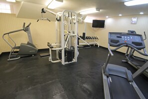 Et fitnesscenter med forskellig træningsudstyr, herunder løbebånd, vægtmaskine og håndvægte.