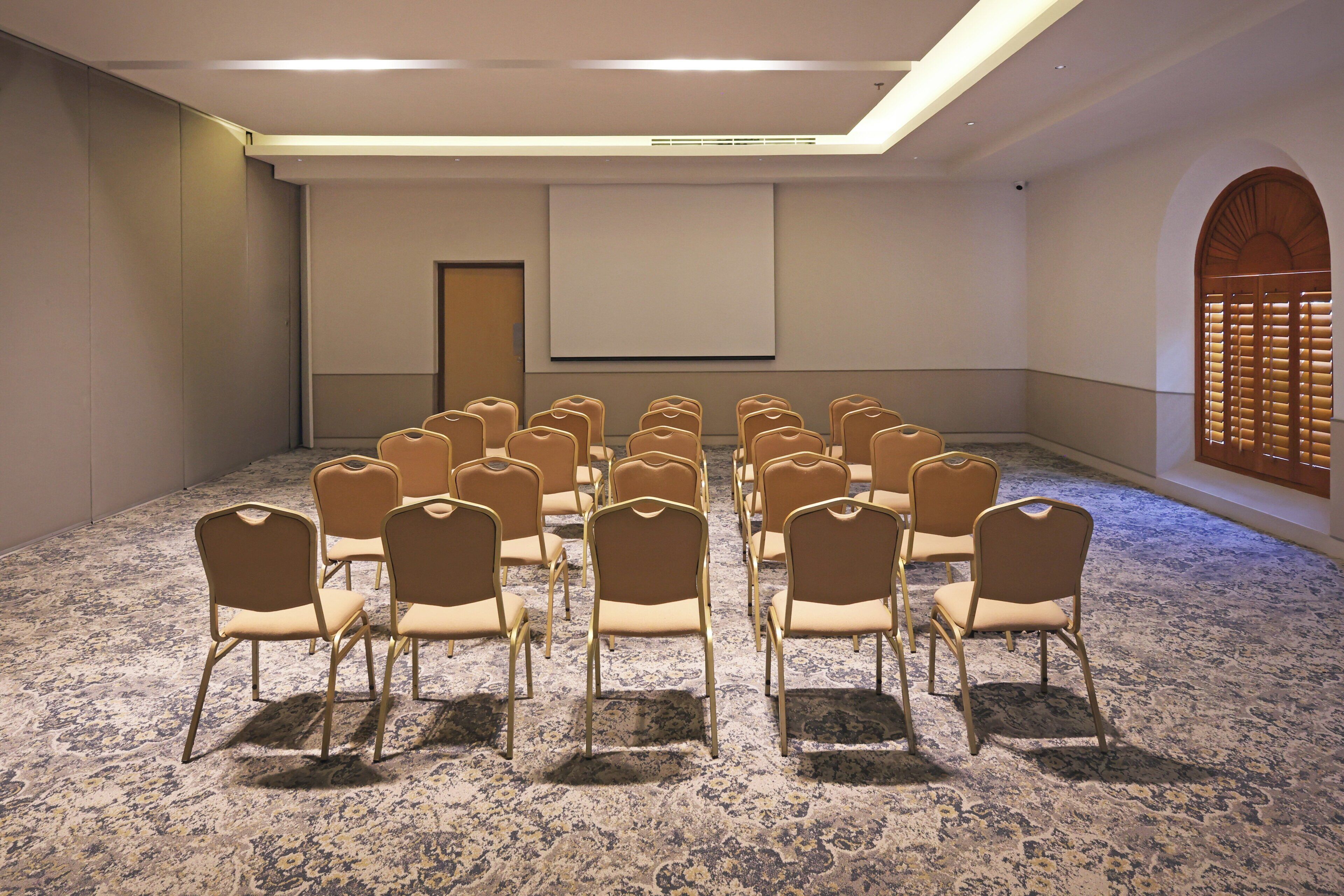 A conference room with rows of chairs, a projector screen, and a carpeted floor.