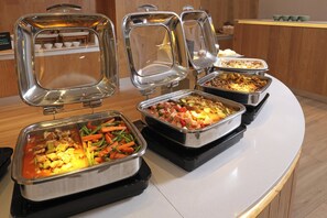 Buffet com diversos alimentos dispostos em bandejas de metal.