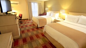 Una habitación de hotel con dos camas, un escritorio con computadora, un televisor y una silla.