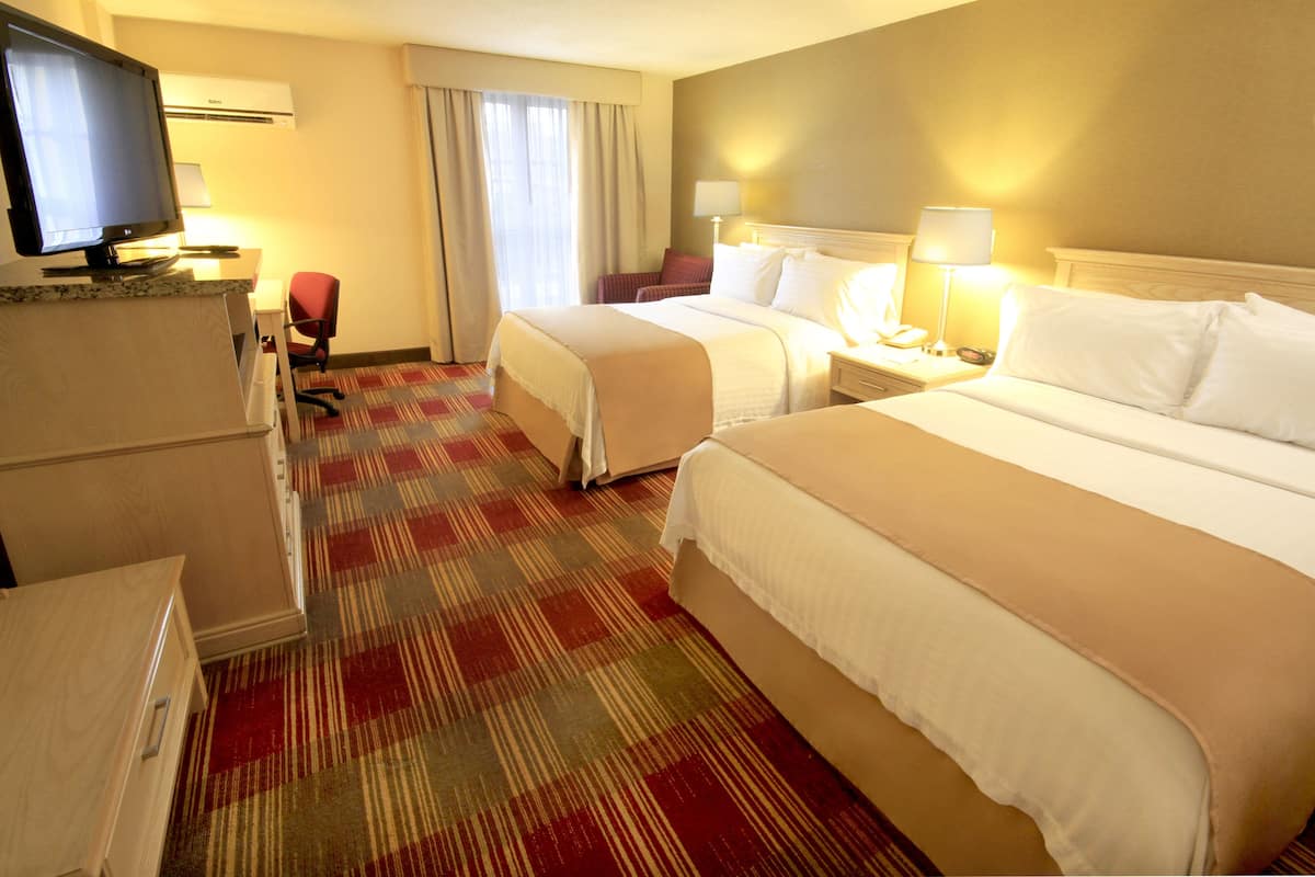 A hotel room with two beds, a desk with a computer, a TV, and a chair.