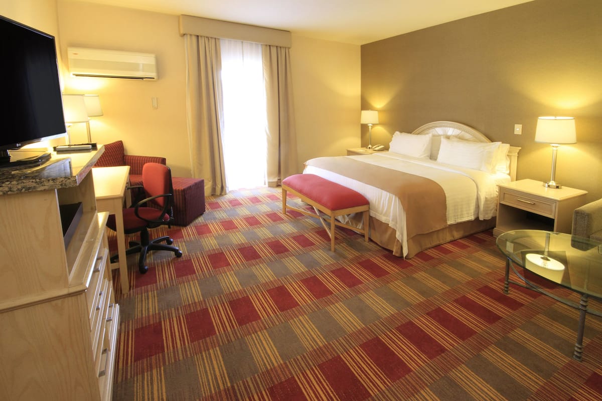 A hotel room with a bed, desk, chair, and a television.