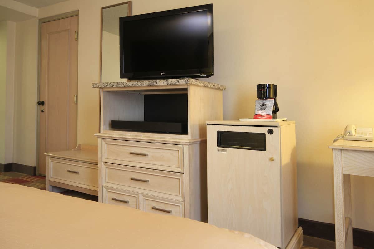 A hotel room with a bed, a television mounted on a cabinet, a coffee maker, and a telephone on a side table.