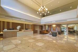 A hotel lobby with a reception desk, seating area, chandelier, and a dining area. - Holiday Inn Monclova by IHG (Monclova)