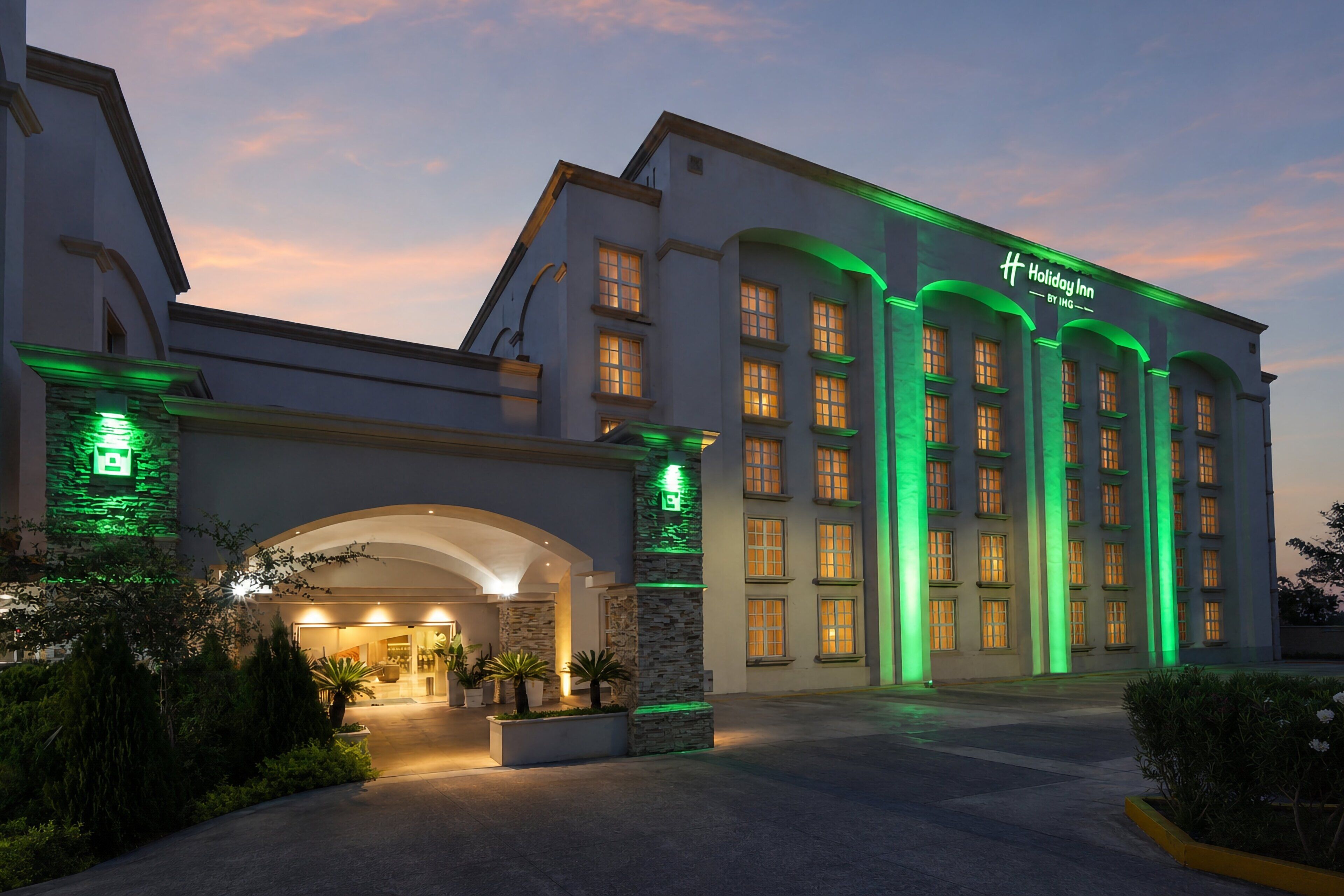 Un hotel con un amplio vestíbulo, numerosas ventanas y detalles de iluminación verde.
