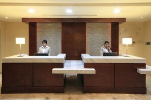 Una mesa de recepción con dos recepcionistas, una encimera de mármol y un panel de madera decorativo.