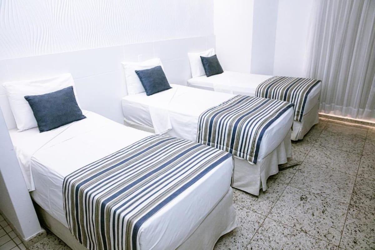 Habitación de hotel con tres camas individuales, cada una con colcha a rayas y ropa de cama blanca.