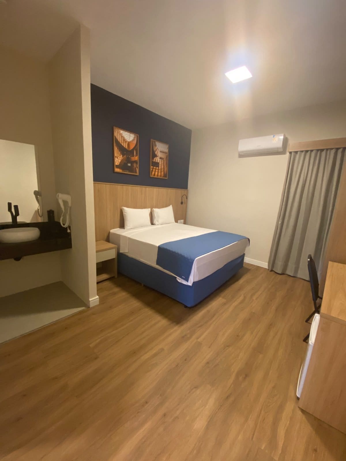 Habitación de hotel con cama, mesita de noche, espejo y aire acondicionado de pared.