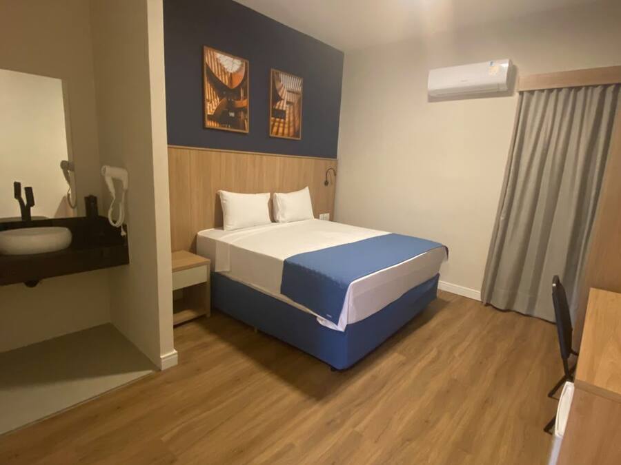 Habitación de hotel con cama, mesita de noche, espejo y aire acondicionado de pared.