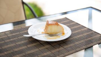 A slice of flan on a white plate with a fork on a glass table with a woven placemat.