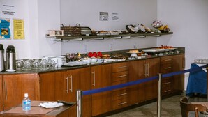 Disposición de un bufé con diversos alimentos y utensilios sobre una barra, rodeada de armarios de madera y una barrera de cuerda azul.