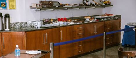 A buffet setup with various food items and utensils on a counter, surrounded by wooden cabinets and a blue rope barrier.