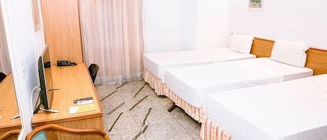 Una habitación de hotel con dos camas individuales, un escritorio con computadora, una silla y un ventanal con cortinas.