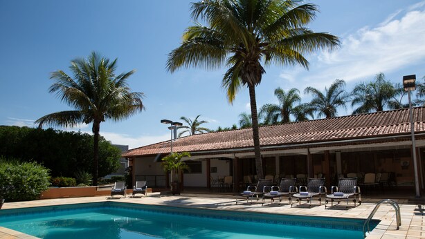 Una piscina con sillas de descanso, palmeras y un edificio con techo de tejas.