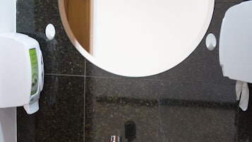 A bathroom with a round mirror, a sink, and a soap dispenser.