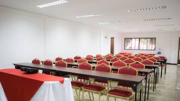 A conference room with rows of tables and red chairs, white walls, and ceiling lights.