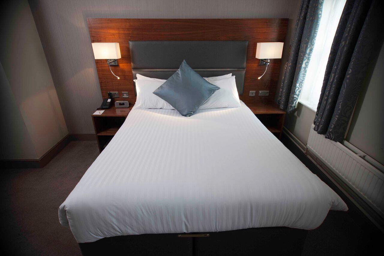 A hotel room with a large bed, two bedside lamps, a nightstand, and a window with curtains.
