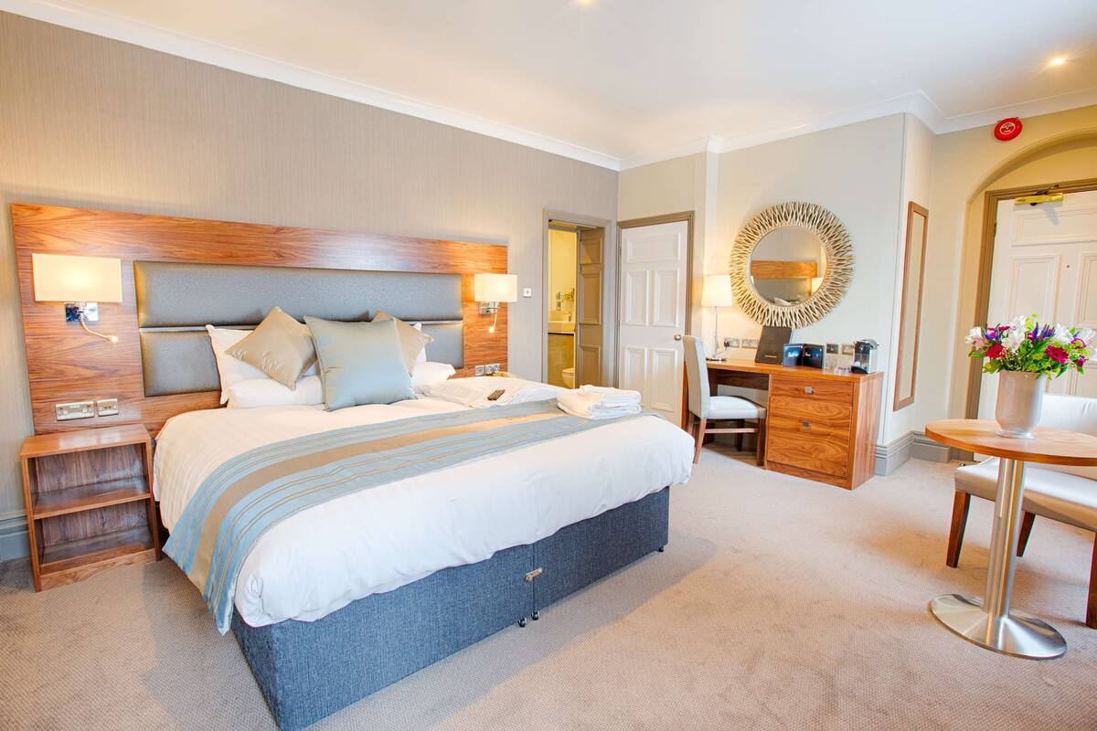 Une chambre d’hôtel avec un grand lit, des tables de chevet, un bureau, une chaise, une commode et un miroir.