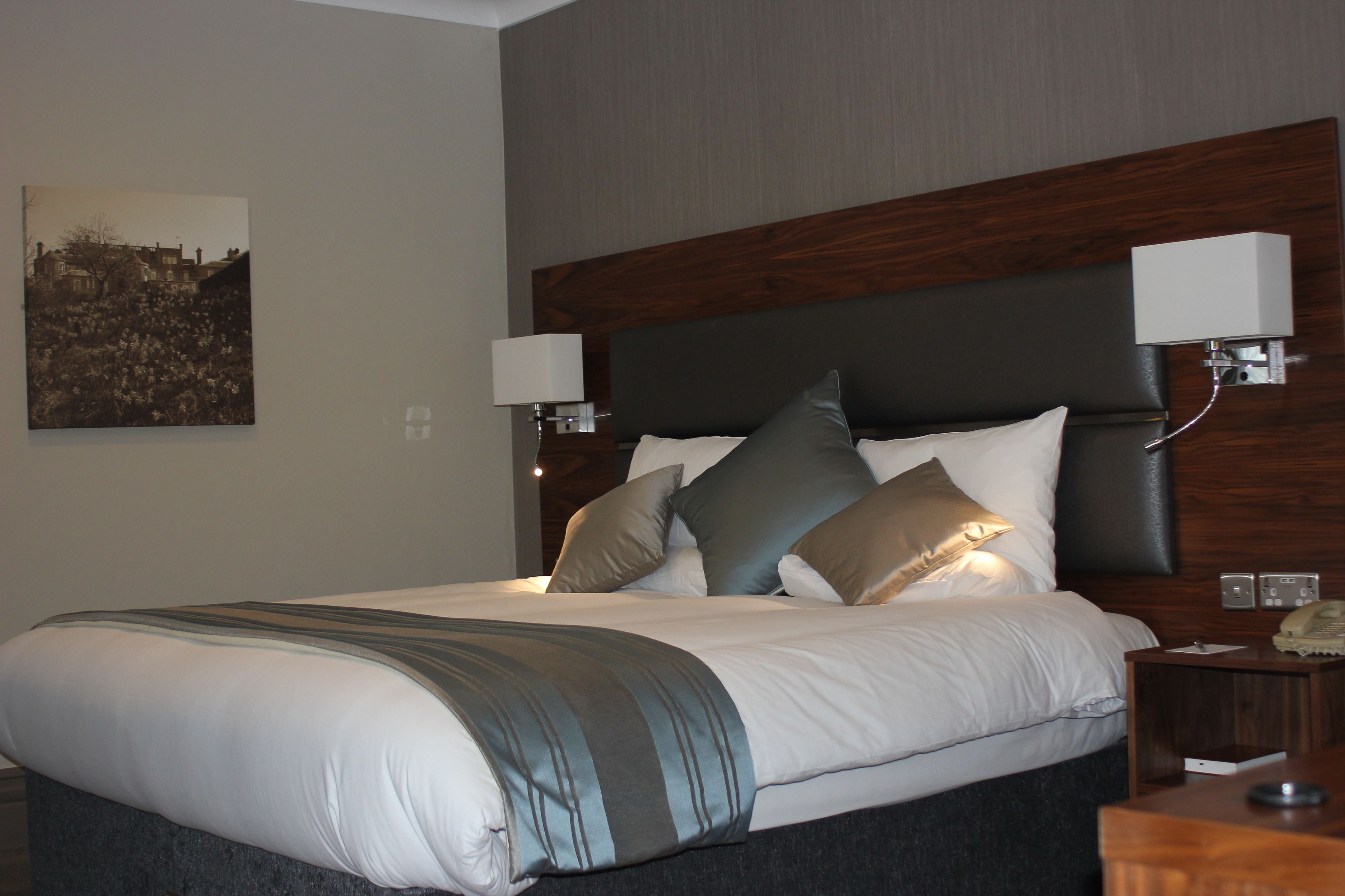 A neatly made bed with a dark headboard, two bedside lamps, and a framed picture on the wall.