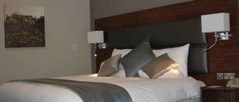 A neatly made bed with a dark headboard, two bedside lamps, and a framed picture on the wall.