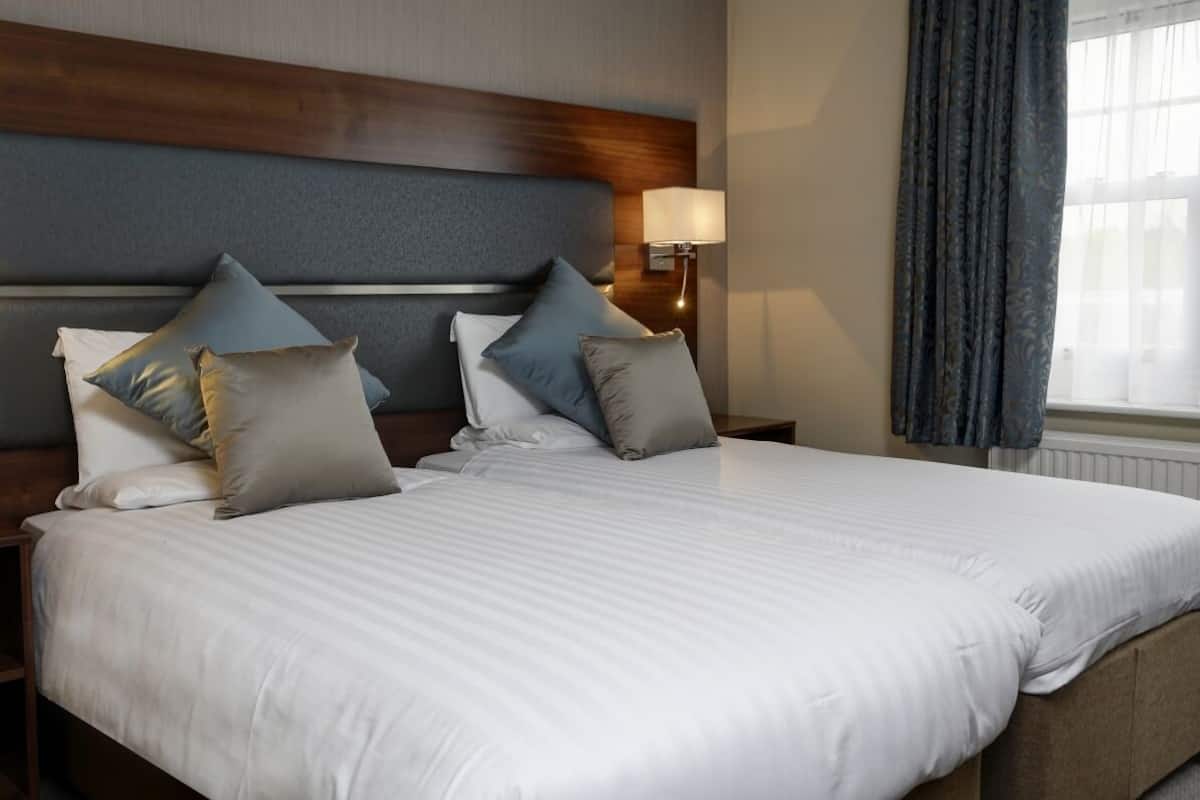 Une chambre d’hôtel avec un grand lit, une tête de lit en bois, une table de chevet avec une lampe et une fenêtre avec des rideaux.