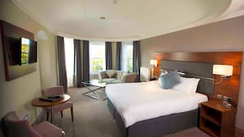 A hotel room with a large bed, a sofa, a small table, a TV, and a window with curtains.