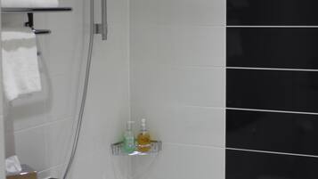 A modern bathroom with a shower, a bathtub, and a toilet. There are white tiles on the walls and a black tiled accent wall. A towel is hanging on a rack, and there are toiletries on a shelf.
