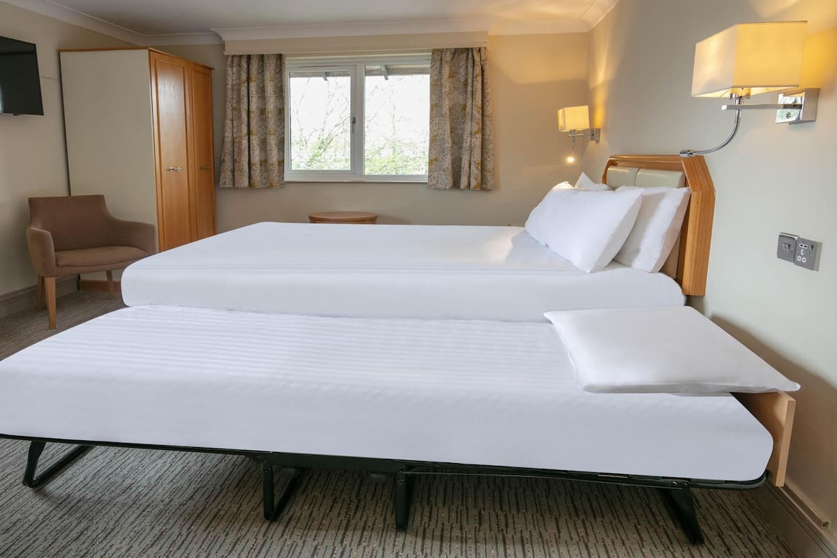 Une chambre d’hôtel avec deux lits, une télévision, une chaise, une fenêtre avec des rideaux et une lampe.