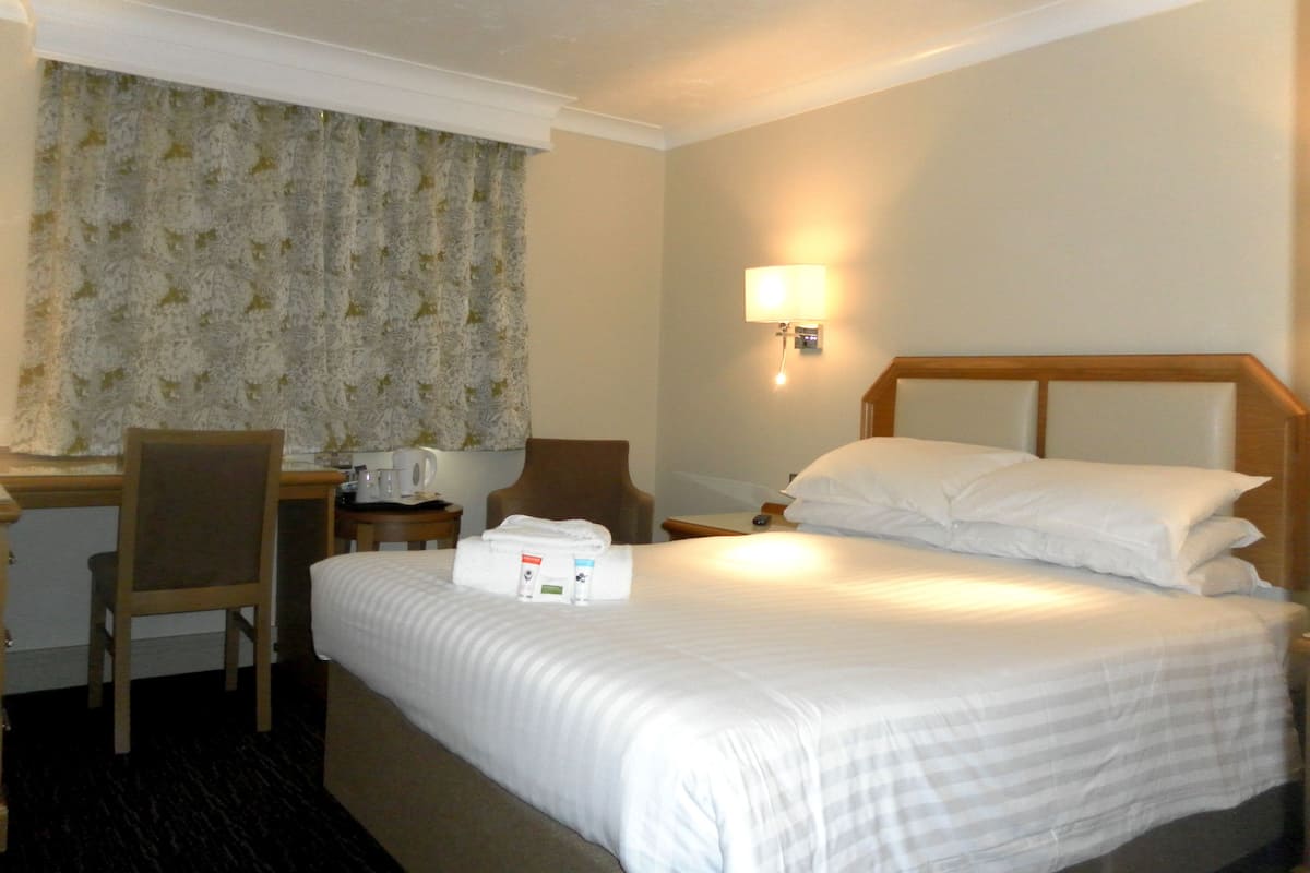 Une chambre d’hôtel avec un lit, un bureau, une chaise, une table de chevet et une lampe.