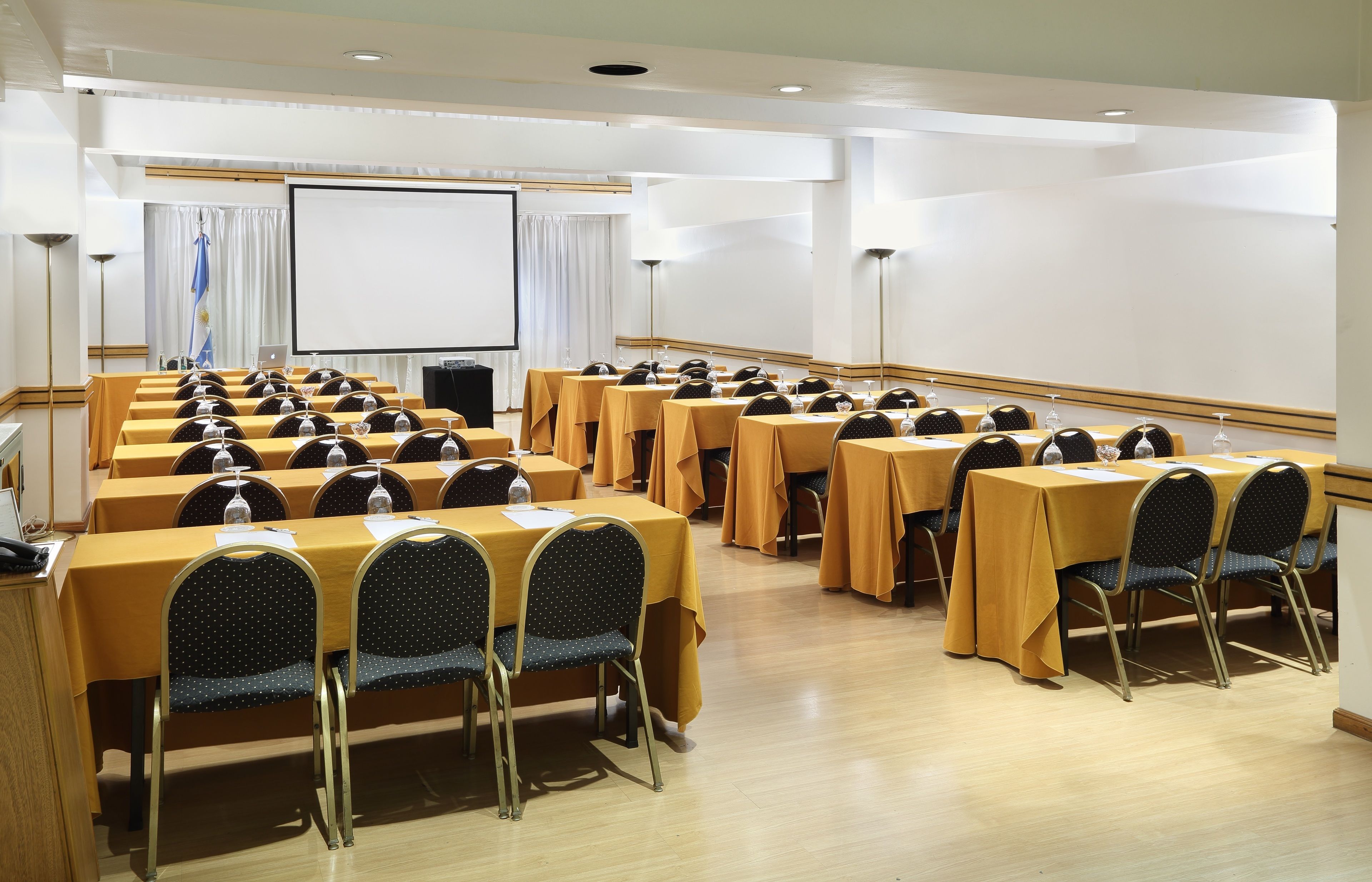 A conference room with multiple tables and chairs, a projector screen, and a podium.
