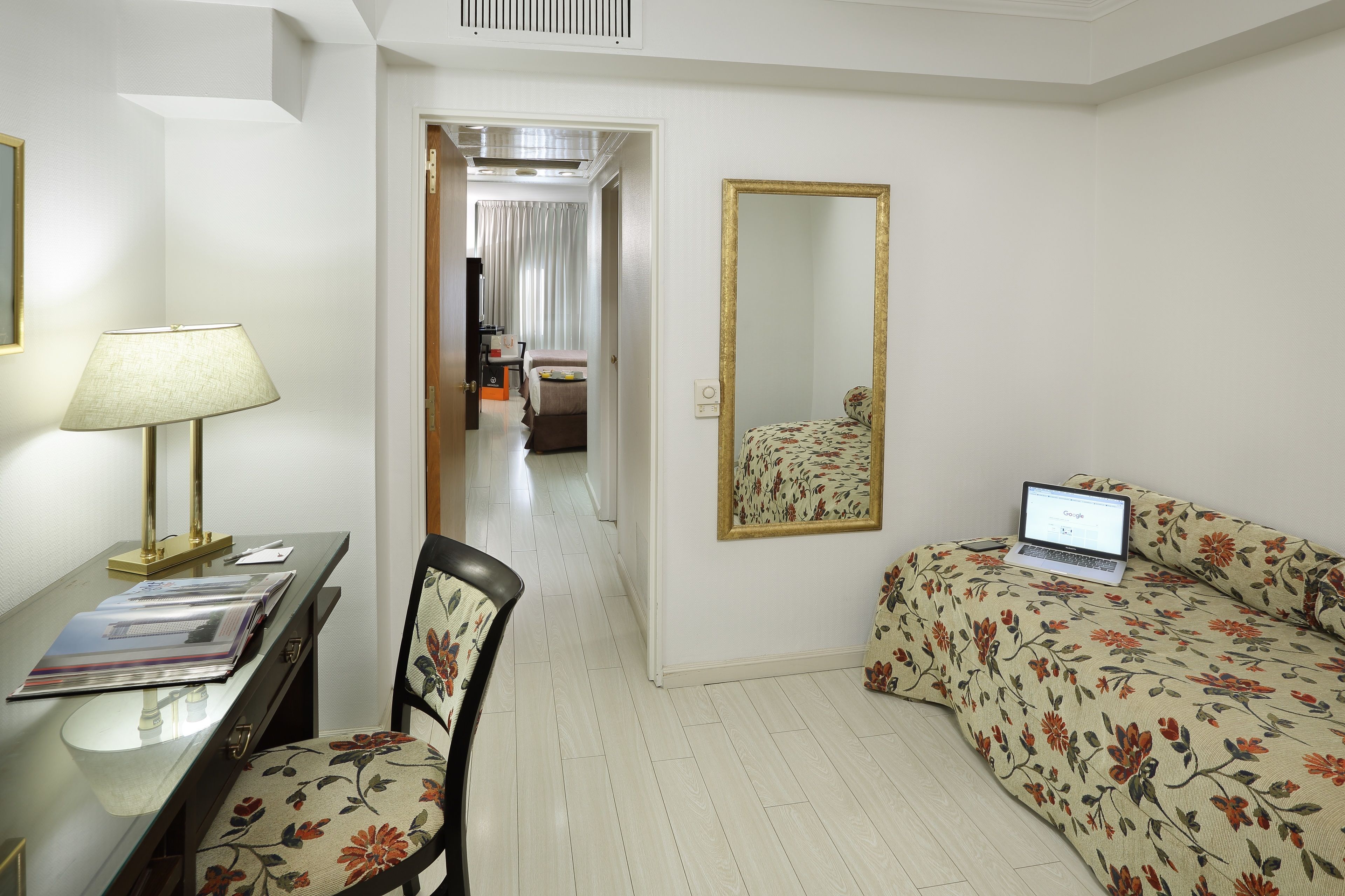 A hotel room with a desk, chair, bed, and a laptop on the bed.