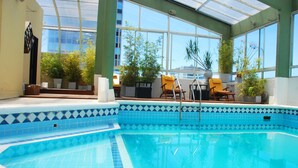 An indoor swimming pool with clear blue water, surrounded by potted plants and yellow chairs. - Dolmen Hotel (Buenos Aires)
