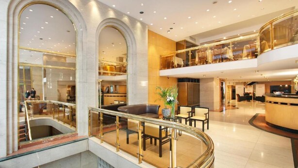 A spacious hotel lobby with a glass railing, seating area, and a second-floor balcony with tables and chairs. - Dolmen Hotel (Buenos Aires)