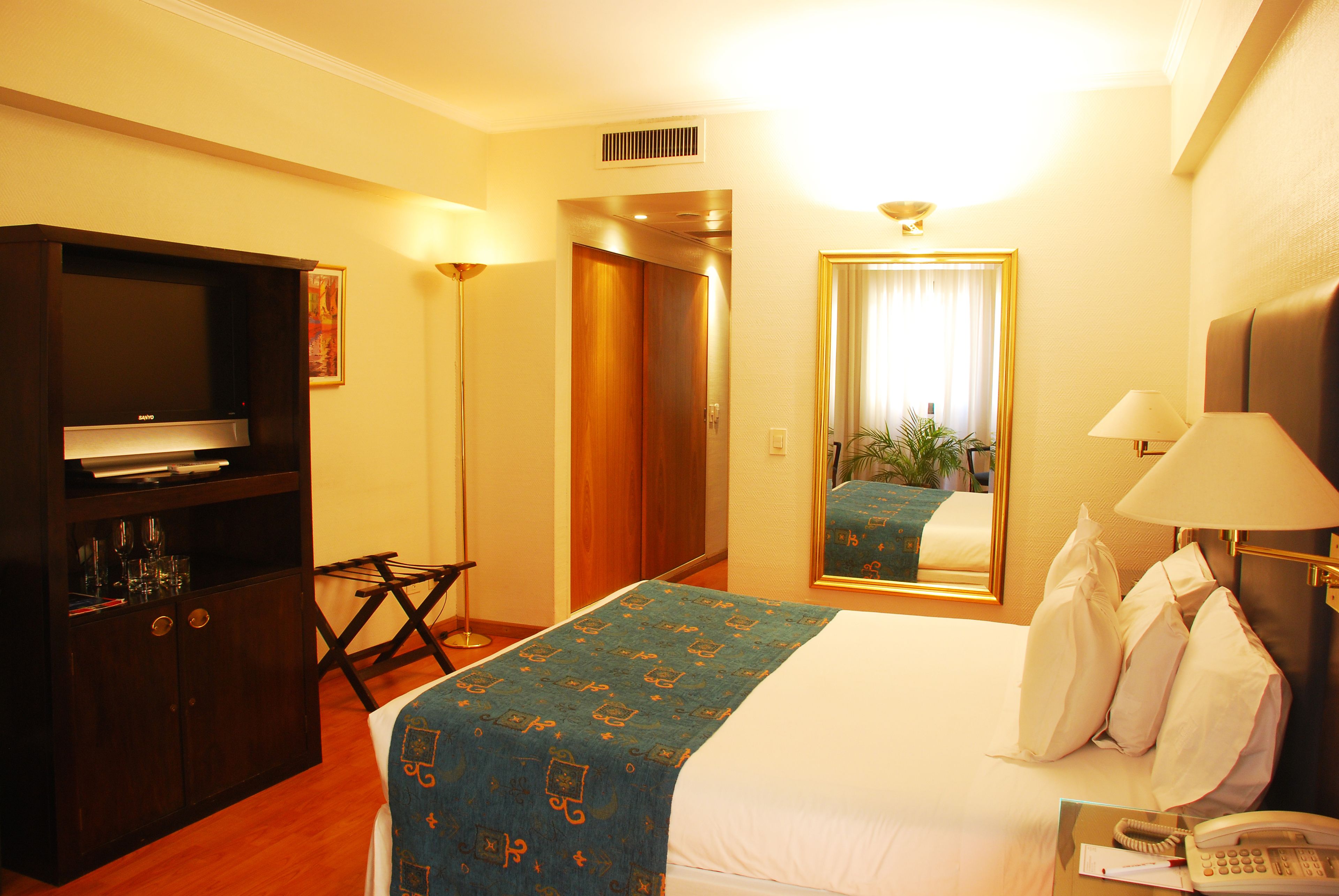 Una habitación de hotel con una cama, televisión, escritorio y espejo.