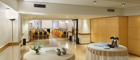 A conference room with multiple tables, a projector screen, and a large wooden partition wall.