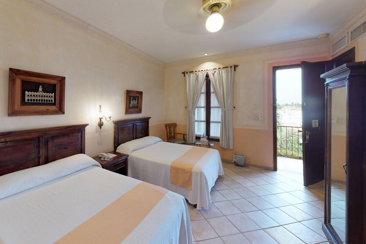 A hotel room with two beds, a nightstand, a lamp, a window with curtains, and a door leading to a balcony.