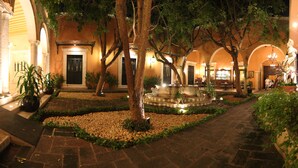 A courtyard with a fountain, trees, and a building with arches and columns. - La Misión de Fray Diego Boutique Hotel (Mérida)