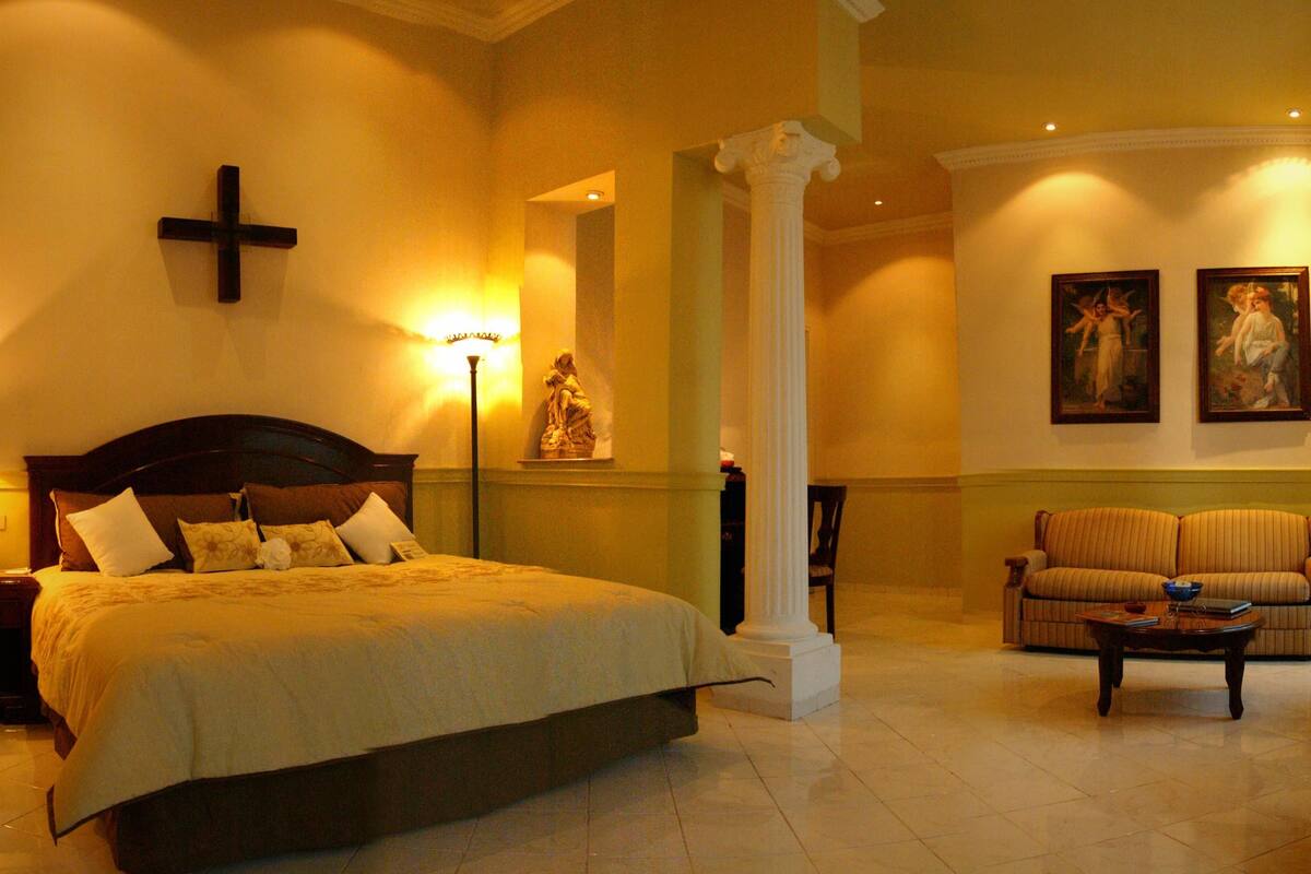 A hotel room with a large bed, a sitting area with a sofa, and a dining table.