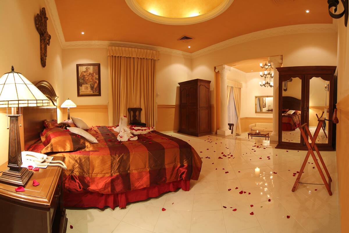 A spacious bedroom with a large bed, a desk with a telephone, a mirror, and a chandelier.
