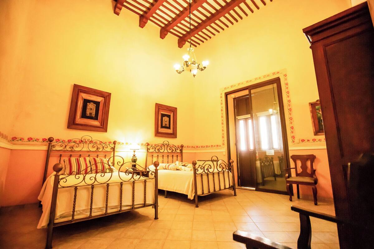 A room with a bed, a chair, a wooden cabinet, and a chandelier.