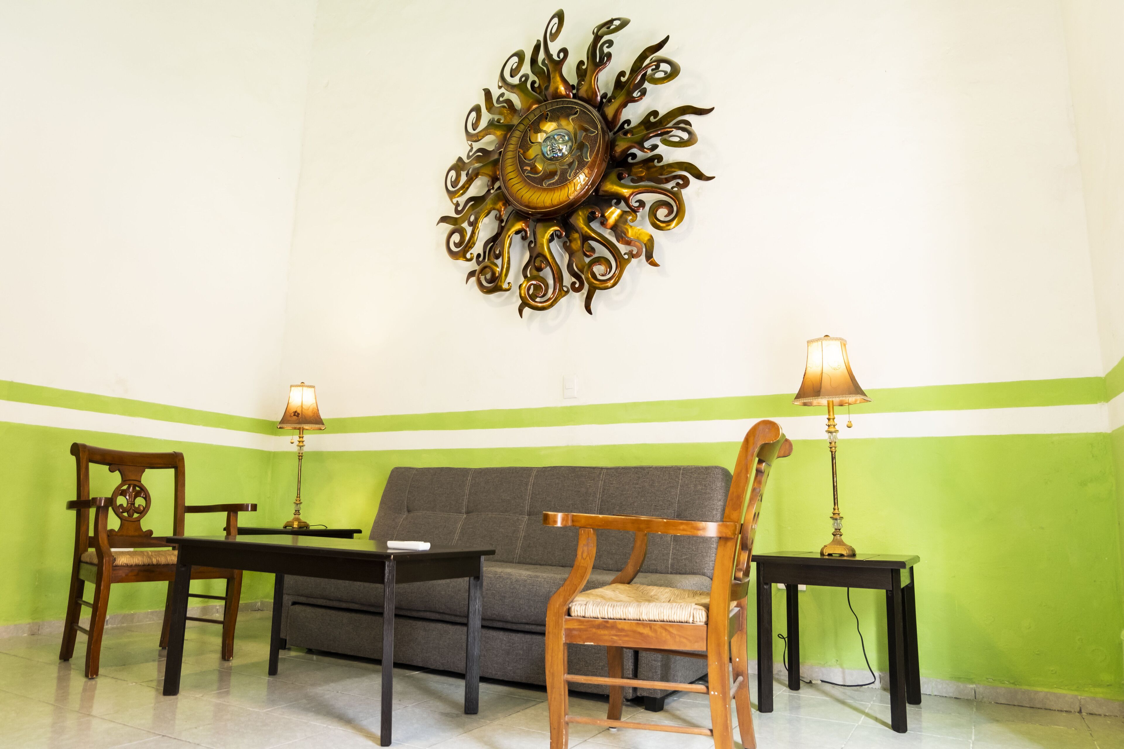 A room with a green and white wall, a sofa, two wooden chairs, a small table, and two lamps.