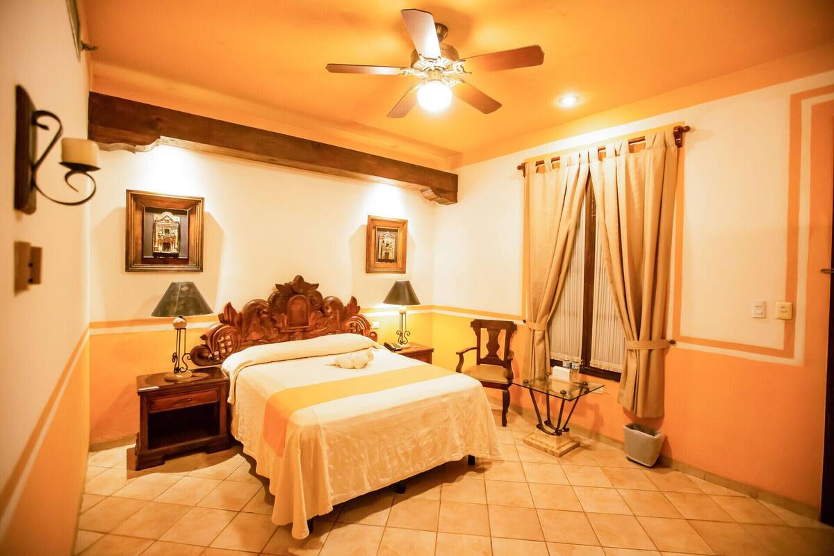 A hotel room with a bed, bedside tables, a ceiling fan, and curtains.