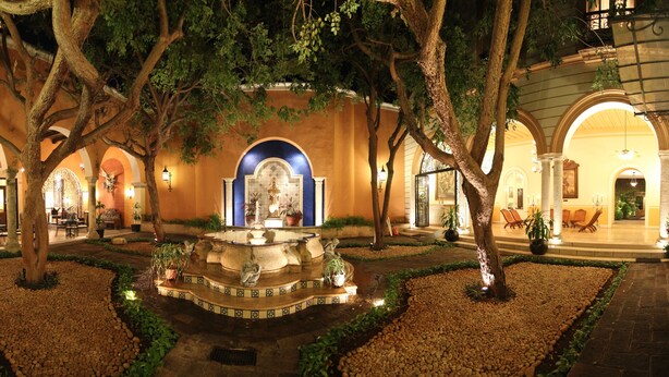 A courtyard with a fountain, trees, and a bar area. - La Misión de Fray Diego Boutique Hotel (Mérida)