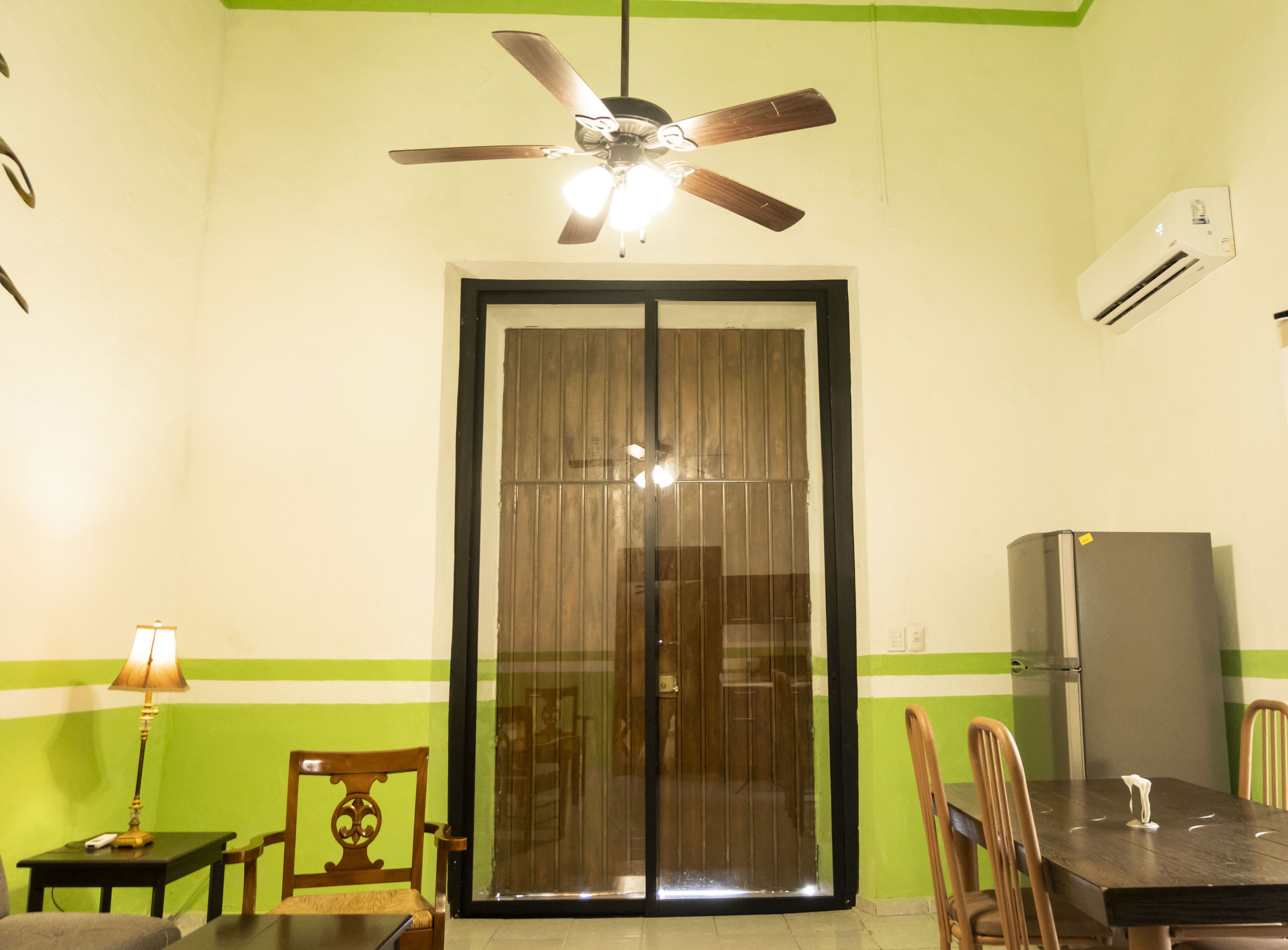 Un comedor con mesa, sillas, ventilador de techo y refrigerador.