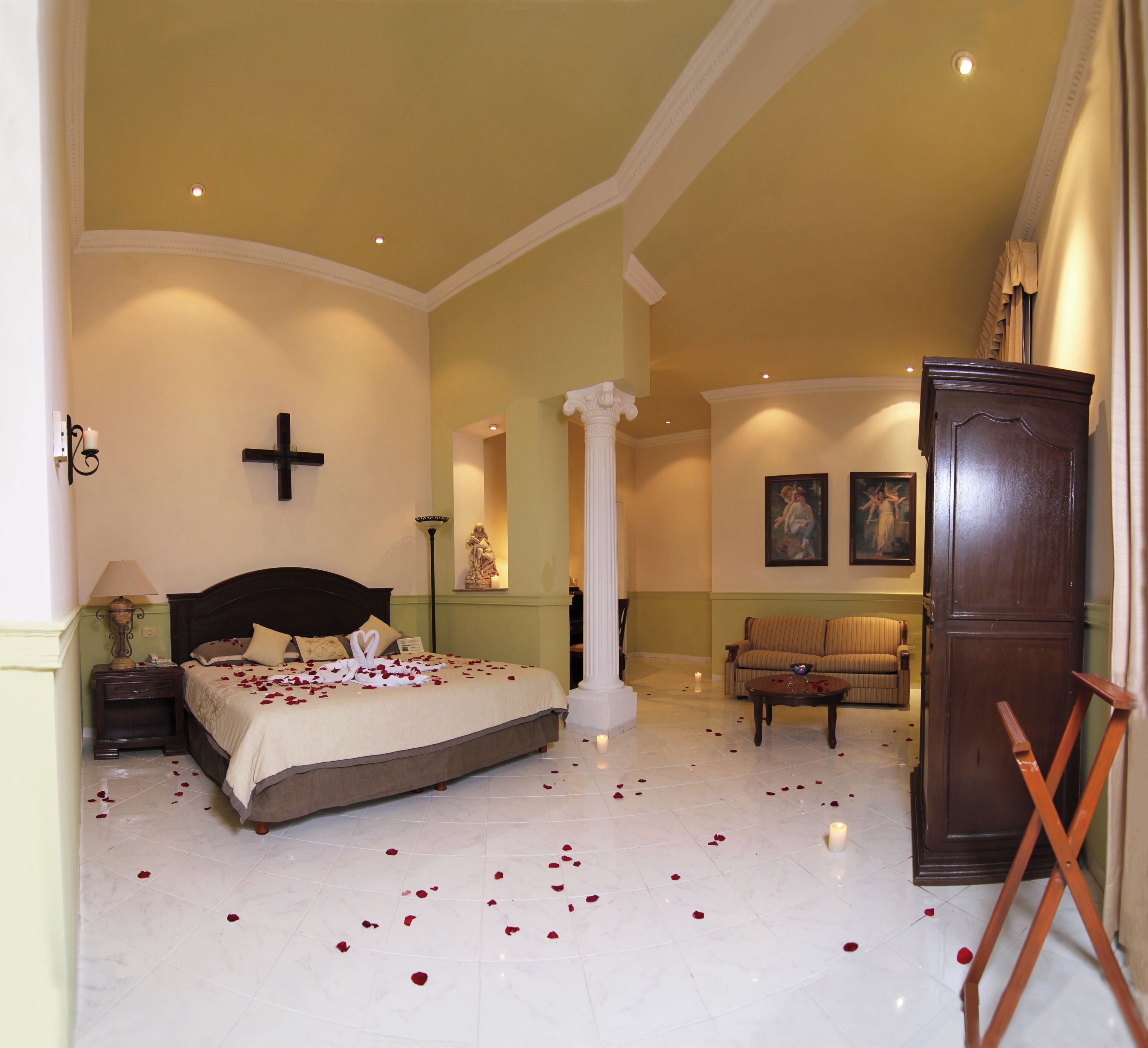 A spacious bedroom with a large bed, a sofa, a cabinet, and a painting on the wall.