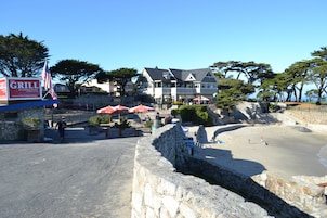 A beachfront property with a stone retaining wall, a restaurant named 'The Grill' with outdoor seating, and a large house with multiple windows and a balcony overlooking the beach.