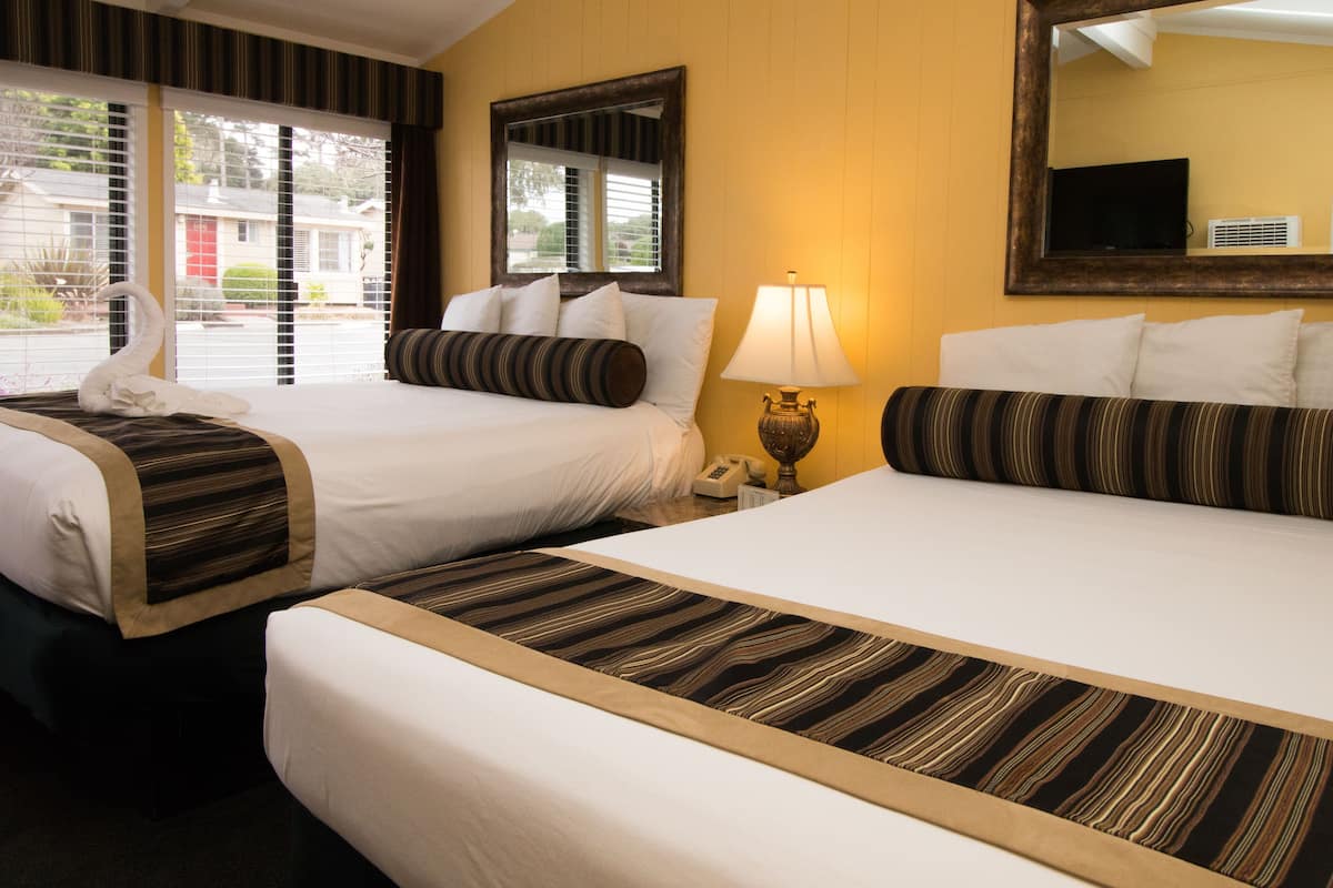 A hotel room with two beds, a large mirror, a lamp, and a view of the outside.