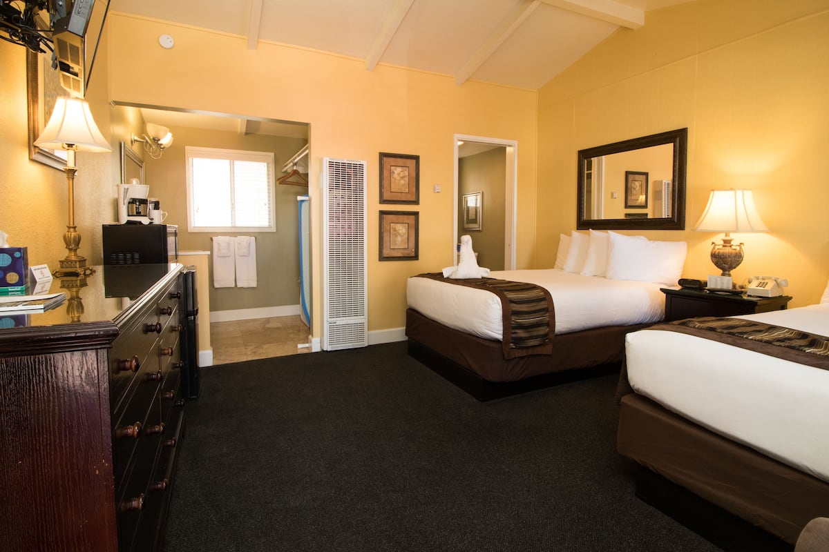 A hotel room with two beds, a desk, a lamp, a coffee maker, and a mirror.