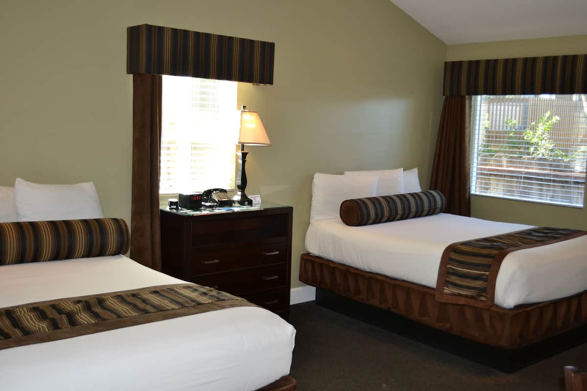 A hotel room with two beds, a desk with a lamp, and a window with blinds.
