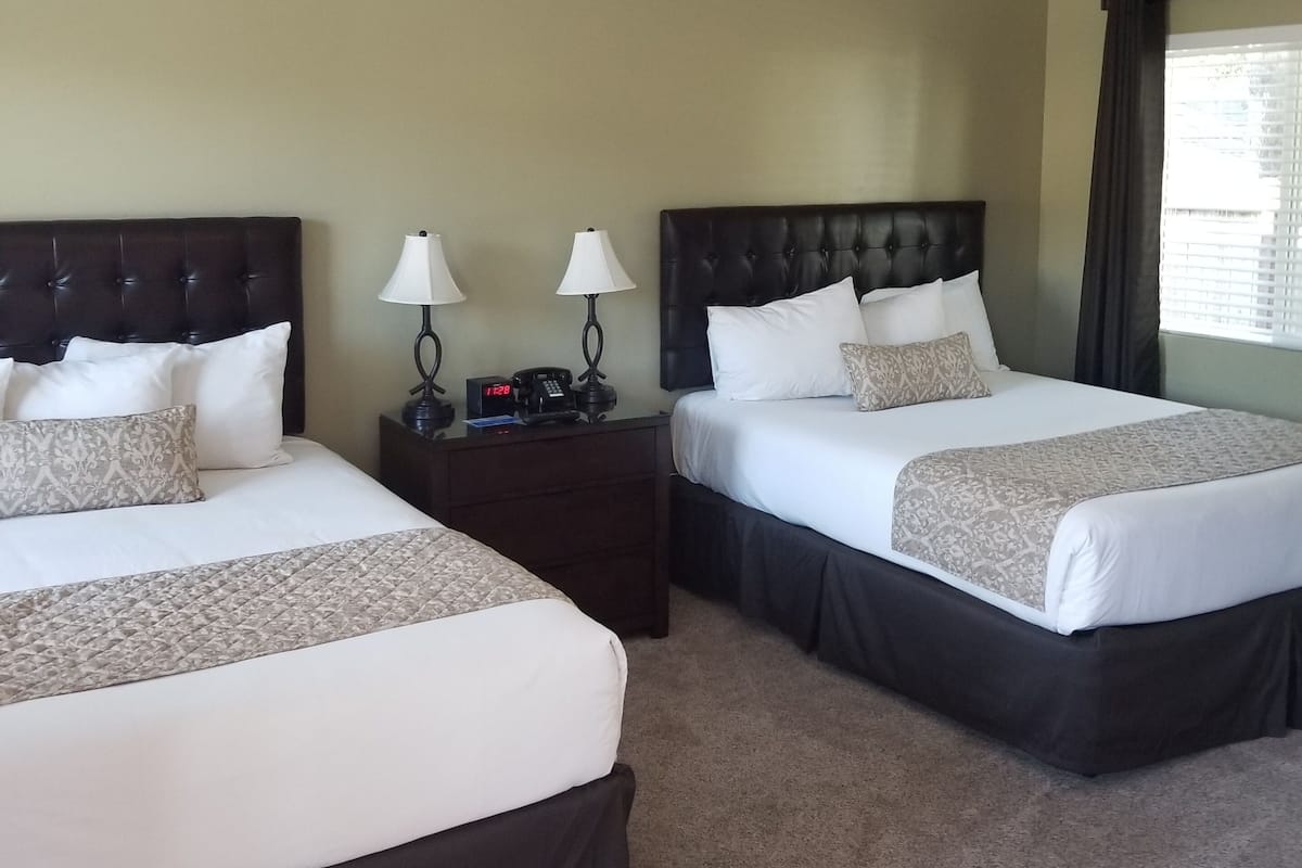 Two queen beds with dark headboards, white linens, and a bedside table with lamps.